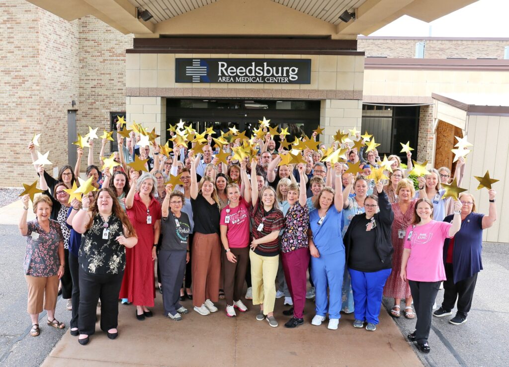 Group of hospital staff outside Reedsburg Area Medical Center, raising gold star props and smiling at the camera