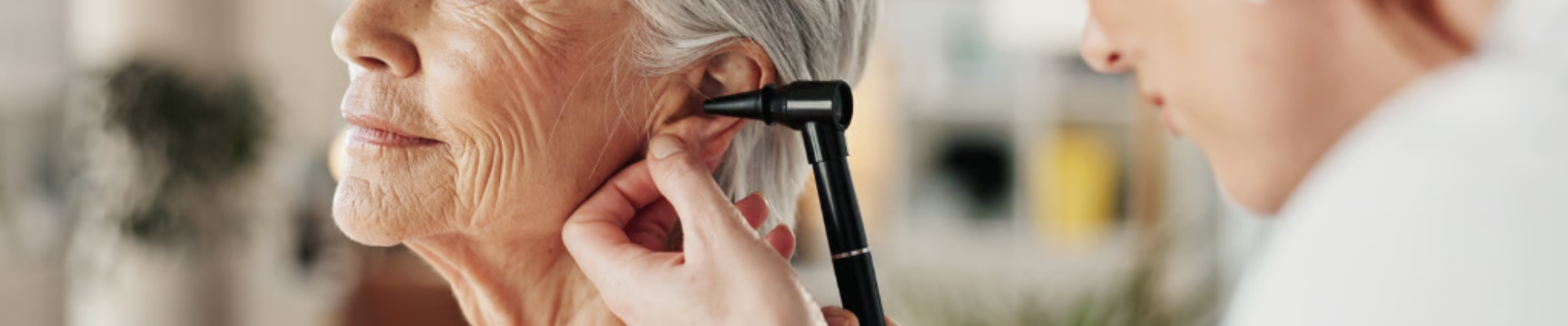 Healthcare professional examines an elderly woman's ear using an otoscope.