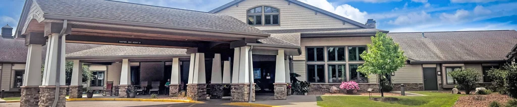 Front entrance of a modern healthcare or senior living facility with a covered drop-off area and stone accents under a gabled roof.