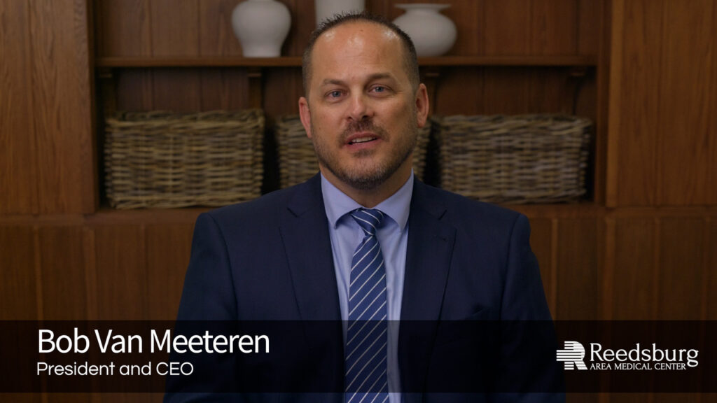 Portrait of Bob Van Meeteren, President and CEO of Reedsburg Area Medical Center, in a navy suit in front of a wood bookshelf.