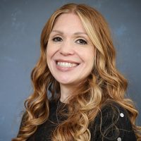 Portrait of a smiling woman with long, wavy light brown hair against a blue background.